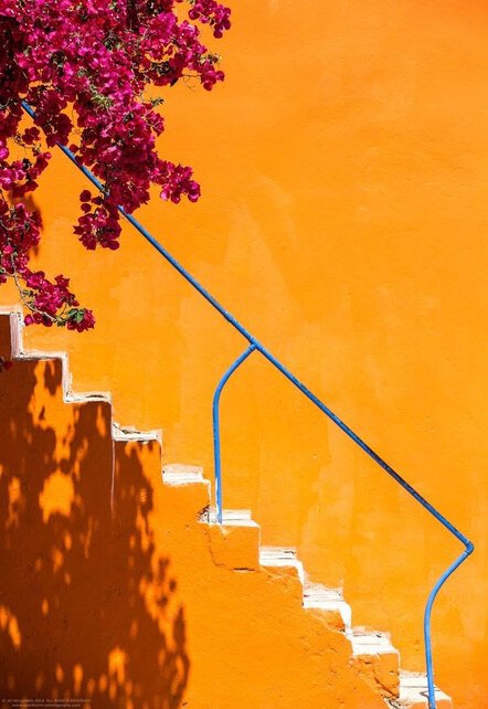 Orange exterior stair with a blue handrail and bougainvillea shadows, used as a colour reference.
